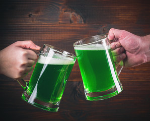 St Patrick's Day concept two mug on hands green beer against wooden background