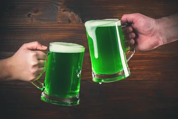 Zelfklevend Fotobehang St Patrick's Day concept two mug on hands green beer against wooden background © Ievgenii Meyer