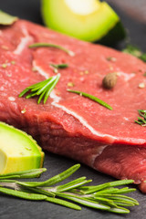 Fresh raw beef meat with avocado and herbs on the black stone background