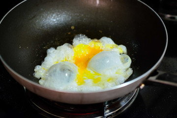 Fresh egg in hot oil on black cooker