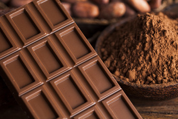 Chocolate bar, candy sweet, cacao beans and powder on wooden background