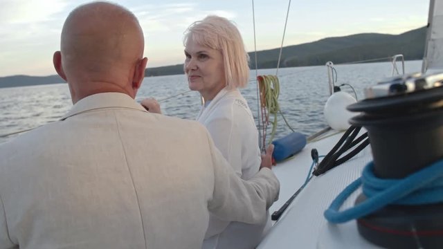 Beautiful senior lady speaking with her husband while cruising on boat along coast