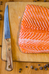 Orange raw fillet of salmon on wooden table with knife and papper
