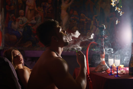 Young sexy athletic tattooed man smoking hookan