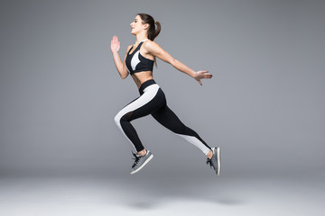 Side view of a sporty young woman jumping isolated on grey background