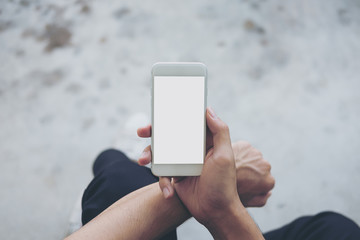 Mockup image of a man sitting on the street and holding white mobile phone with blank white screen   