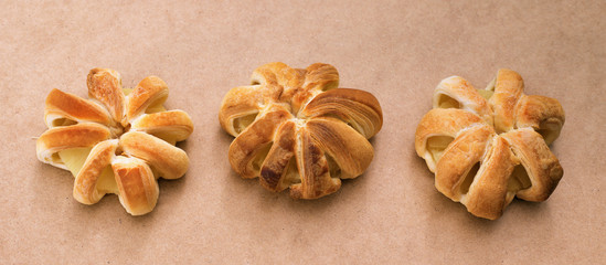 Fototapeta na wymiar Three confectionery products buns with pineapple inside lie in a row on a light brown natural background. Baked puff pastry rings of pineapple.