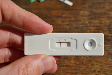 Male hand holding a female pregnancy test with two stripes as a positive confirmation of baby expectation above wooden background