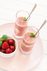 Two glasses with fresh strawberry and banana smoothie decorated mint leaves on white wooden background. Selective focus
