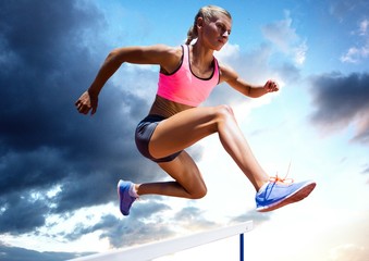 Fototapeta na wymiar Athlete jumping over a hurdle against sky in background