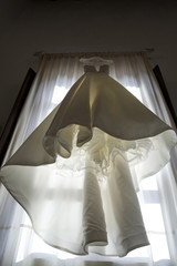 abito da sposa visto dal basso appeso su tenda in controluce