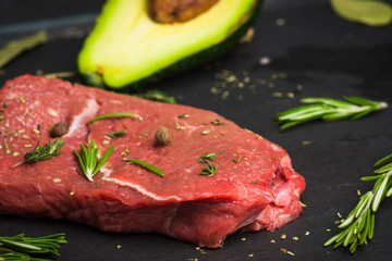 Fresh raw beef meat with avocado and herbs on the black stone background