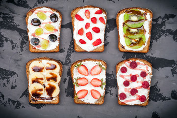 Healthy breakfast. Sweet sandwiches with cream cheese and fresh berries and fruit on dark background. Toasts for breakfast. Top view