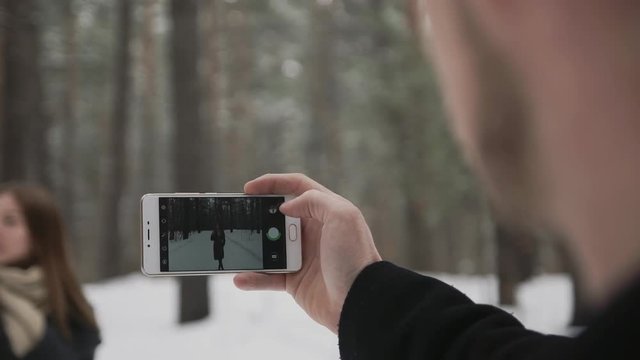 couple is taking pictures, man photographing his girlfriend at cellphone in a snow winter forest