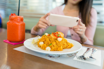 Woman taking photo on fried noodles with cellphone