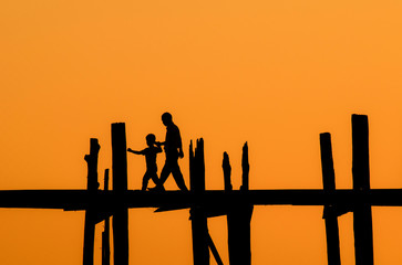 silhouette of tourist father and son crossing the river on the longest bridge in the world, U-Bein Bridge, Mandalay, Myanmar.