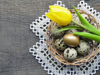 Easter decoration with spring yellow tulip and quail eggs in basket on old wooden background with copy space.Easter eggs.Happy Easter or Spring concept.Selective focus.
