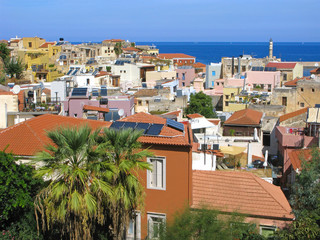 Obraz premium Panorama of Chania old town top view. Old houses with red roofs, Venetian lighthouse. Sailboats in sea and clear sky.
