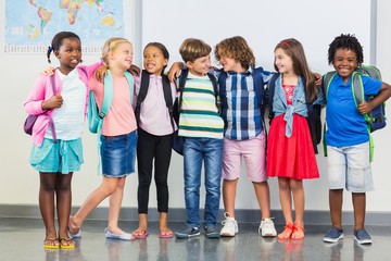 Smiling kids standing with arm around in classroom