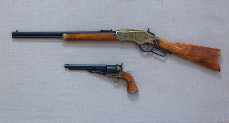 The old rifle and a gun with wooden and metal pieces are on the fabric background.