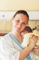 Happy and tired young mother with newborn baby in hospital after giving birth