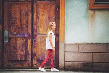 Outdoor fashion portrait of 8-9 year old girl walking down the street, wearing polkadot trousers and white tee shirt, toned image