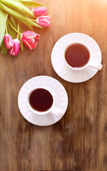 Pink tulips on wooden background, two cups of tea and coffee on saucers with hearts marmalade
