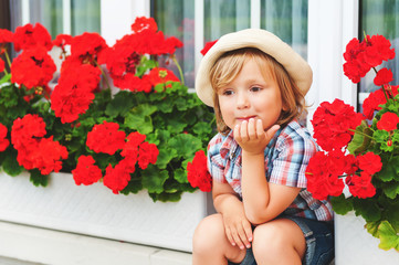 Adorable little boy gardener sitting between bright red geranium in pots