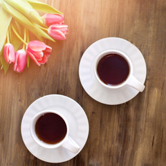 Pink tulips on wooden background, two cups of tea and coffee on saucers with hearts marmalade