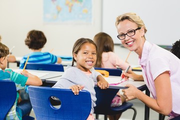 Smiling teacher helping kids with their homework in classroom