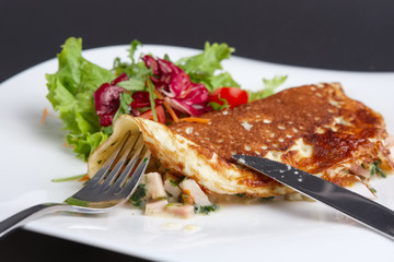 Cutting with knife omelet with ham and vegetables