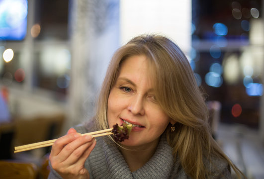 Blonde woman has dinner in japanese restuarant  with sushi and drink red wine