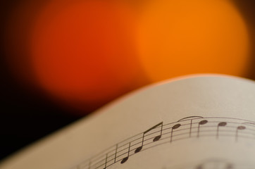 Abstract image with partiture sheet with music notes and blurred fireplace for background.