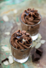 Chocolate mousse with chocolate sauce and chocolate pieces, almond slices in a glasses on a vintage background.
