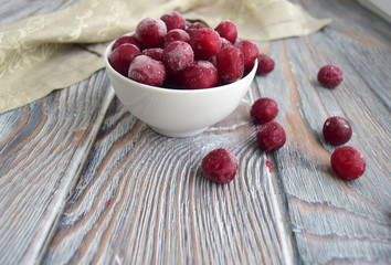 Замороженные вишни лежат в тарелке. Тарелка находится на деревянном столе .  Натуральные продукты природы. Вишни покрыты инеем.
