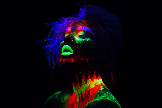 Beautiful extraterrestrial model woman with blue hair and green lips in neon light. It is portrait of beautiful model with fluorescent make-up, Art design of female posing in UV with colorful make up