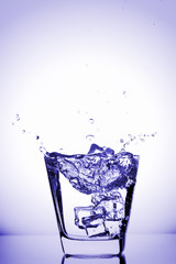 Ice cubes splashing into glass, ice cube dropped into glass of water, fresh, cold water, isolated on violet, blue  background.
