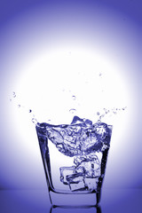 Ice cubes splashing into glass, ice cube dropped into glass of water, fresh, cold water, isolated on blue background.