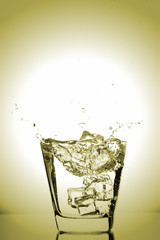 Ice cubes splashing into glass, ice cube dropped into glass of water, fresh, cold water, isolated on gold, yellow, bronze  background.