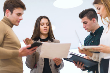 Group of people standing close to each other while and gesturing. Group of students preparing for exams discuss in the hall.