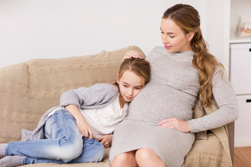 happy pregnant woman and girl on sofa at home