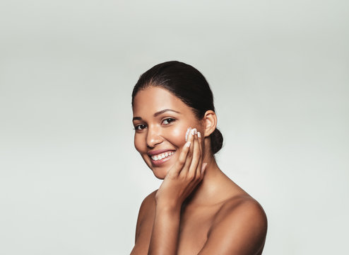 Fototapeta Smiling woman applying moisturizer on her face