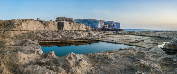 Eroded rocky formation on the waterfront cliff with natural, square water reservoir on the summer evening.