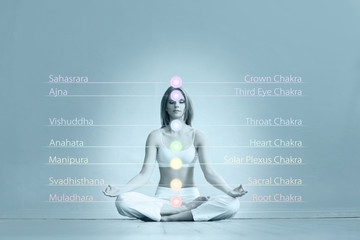 Young and healthy girl meditating in lotus position. Colored chakra lights over her body. Yoga,...