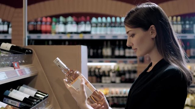 Young Beautiful Woman Chooses Wine In The Supermarket. Brunette in alcoholic shop