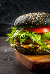 Freshly homemade black burgers with cheese, beef minced steak, tomato and lettuce. On the black...