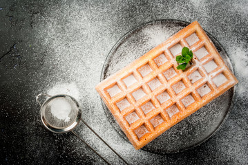 Freshly baked Belgian waffles, sprinkled with powdered sugar. On a black plate on a black stone...