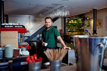 Bartender barista with coffee in hand behind the bar at the break.