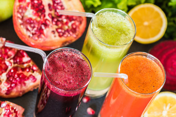 three glasses of different fresh juice. Beet, carrot and kiwi juices on grey background