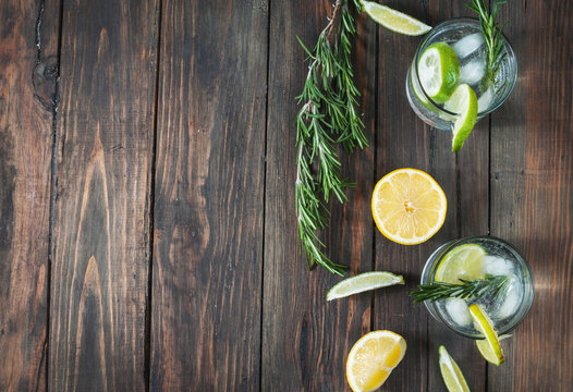 Alcoholic drink gin tonic cocktail with lemon, rosemary and ice on rustic wooden table, copy space
